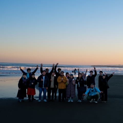 migakiba oaraiのイメージ写真。夕方時、大洗の美しい海を背景にフィールドワークに参加したメンバー16名が前後２列で写っています。