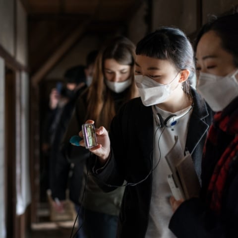 migakiba ozuのイメージ写真。フィールドワークで、参加者が改修された古民家を見学し、スマートフォンで撮影している様子が写っています。