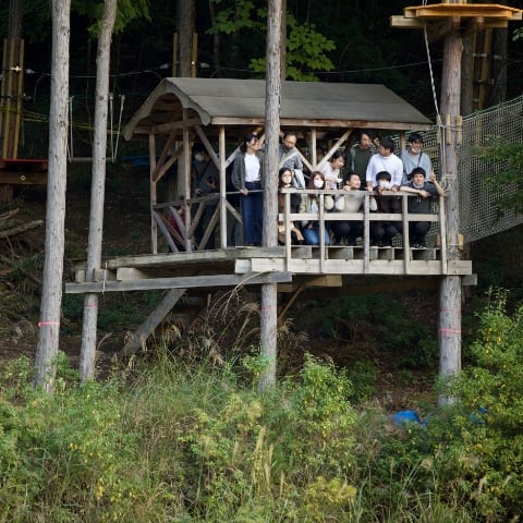 あうる京北のフィールドの「ツクル森」にあるツリーハウスに参加者15名ほどが登って、原っぱを眺めています。