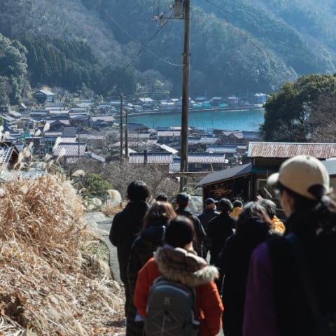 migakiba4期、滋賀県長浜市でのフィールドワークの様子。菅浦の集落で、須賀神社の見学を終えて、琵琶湖に向かって歩く、参加者10名ほどの背中が写っています。