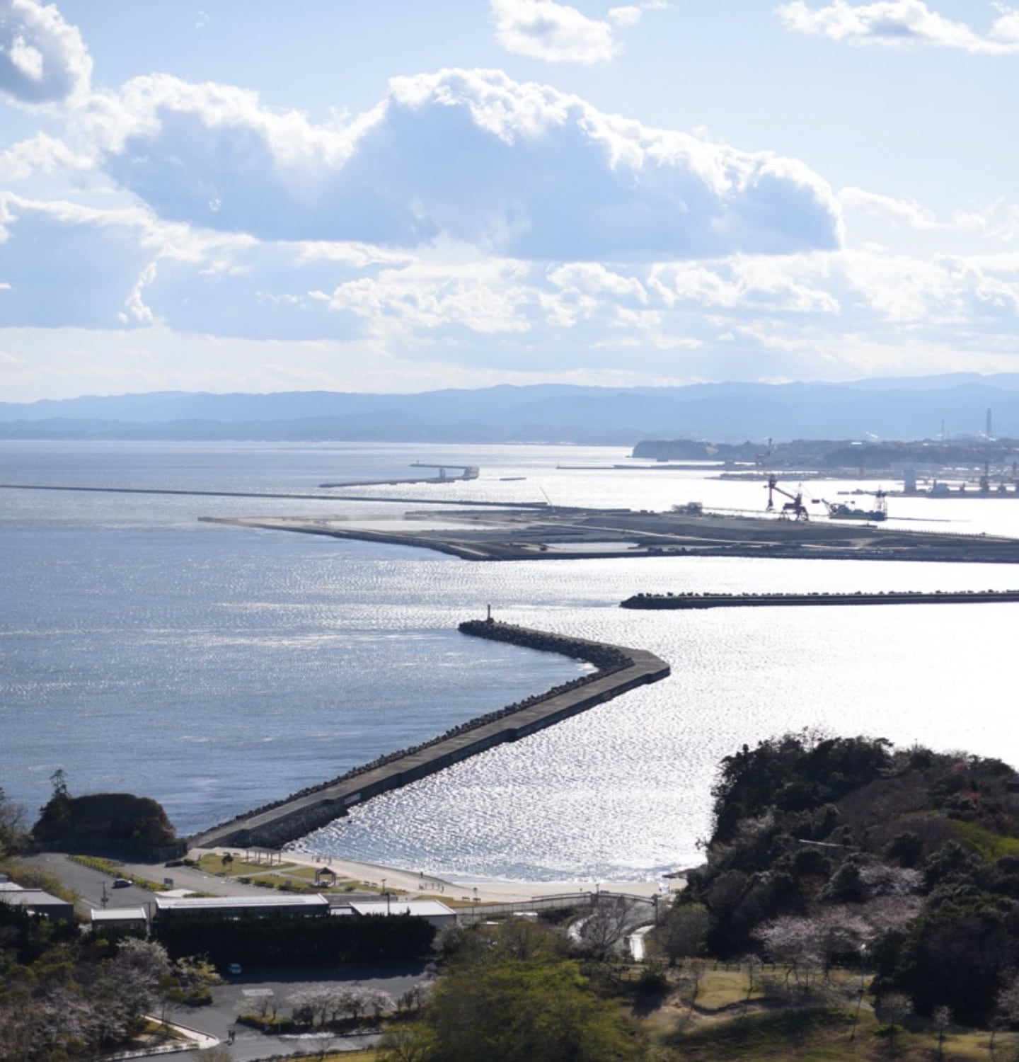 写真：migakiba iwakiのいわき市三崎公園港の見える丘より望む小名浜港の風景。開かれた海の水面に反射する太陽の光と青空の青が混じり合う。右手に小名浜の工業地帯が見えます。