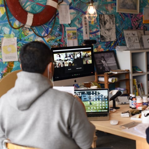 写真：migakiba iwakiで実施したオンライン対話会の様子。現地事務局・現地チームが集合するオルタナティブスペースUDOKに置かれた、パソコンの画面に参加者が話す様子が映し出されています。