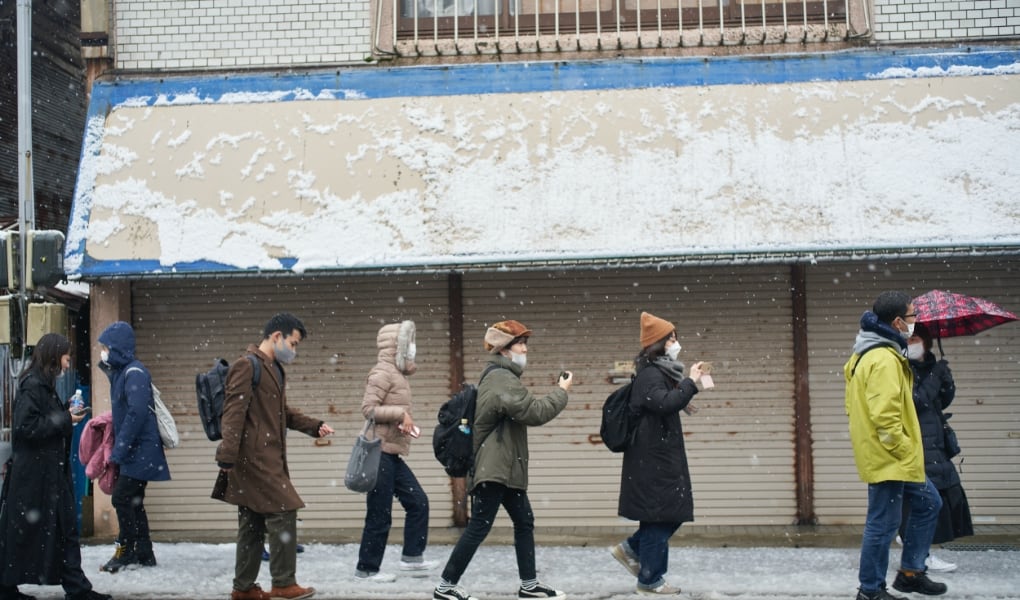 雪の五城目朝市通りを歩くmigakiba参加者を撮影した画像。スマートフォンを手に撮影をしながらフィールドワークを行っている。
