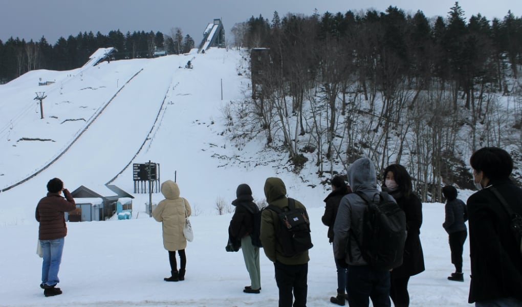 フィールドワーク訪問中の写真です。雪舞う中で、フィールドツアーの参加者が、ピヤシリスキー場のすぐそばにあるスキージャンプ台を眺めています。